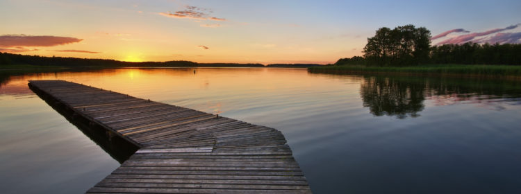 Photo d'un ponton avançant dans l'eau vers l'horizon lors d'un couché du soleil