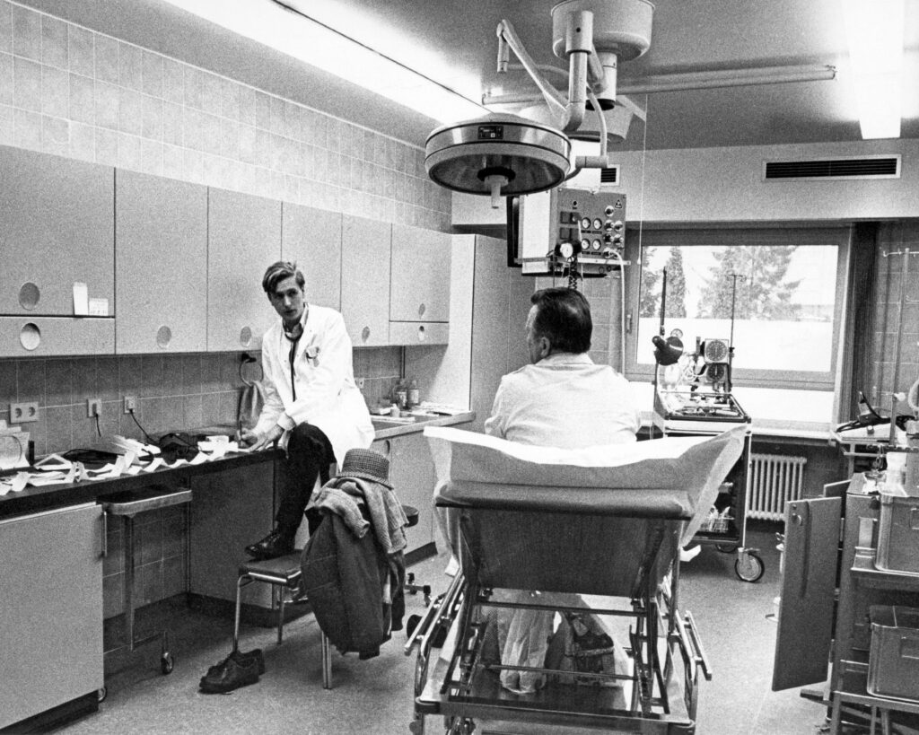 Mir gesinn hei wie di theoretesch Kenntnisser ( hei e Verbandwiessel) an der Praxis an um Patient gemaach gi sinn. D’Material ( Pincette, an Kompressen an Tupfer ) sinn ob engem Inoxplateau preparéiert gi an dann mat den Desinfektiounsmëttelen an Crèmen ass d’Wonn versuergt gi. D’Soignants hunn demols hir Dengschtkleedung selwer gewäsch. D’Bild ass vum Pol Aschmann Fotograph zu Lëtzebuerg.