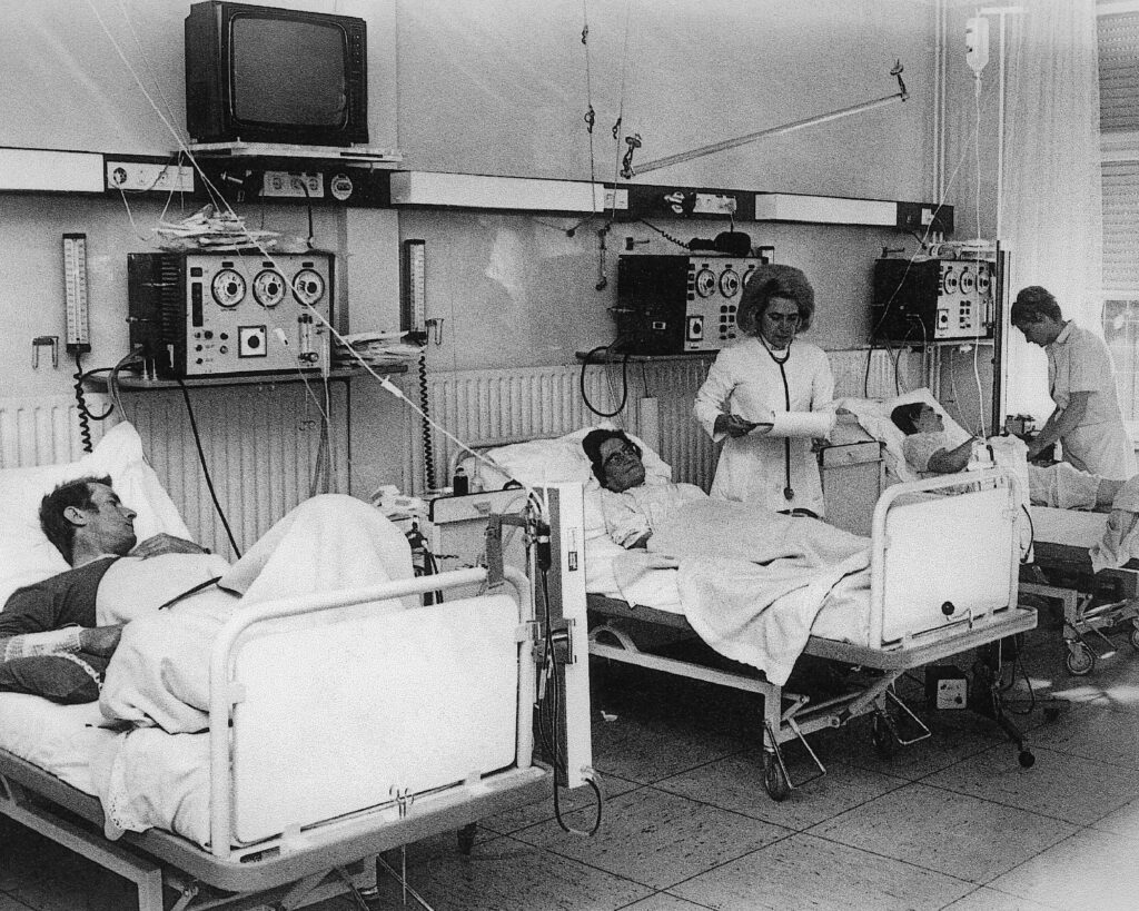 Bild vun der éischter Statioun wou Nierenkranker dialiseiert goufen. Mir gesinn hei di éischt Maschinnen di Nieren ersat hunn. Et gouf zu dëser Behandlung wéineg Alternativen, Transplantatiounen sinn vill spéider komm. D’Patienten sinn e puer mol pro Woch komm an hir d’Blutt ass wärend e puer Stonnen filtréiert gi. D’Soignants woren spezialiséiert ob des Behandlungen, sinn hunn wéinst der grousser Nofro vun Patienten ob Schichte geschafft. Hei woren och di éischt Televisiounen fir Patienten well si iwwert laang Zäit hei a Behandlung woren.Nieft dem Operatiounszëmmer, der Radiologie an dem Laboratoire wor d’Dialyse eng mat deenen ganz techneschen Abteilungen. Weesebild, de Fotograph ass net bekannt.