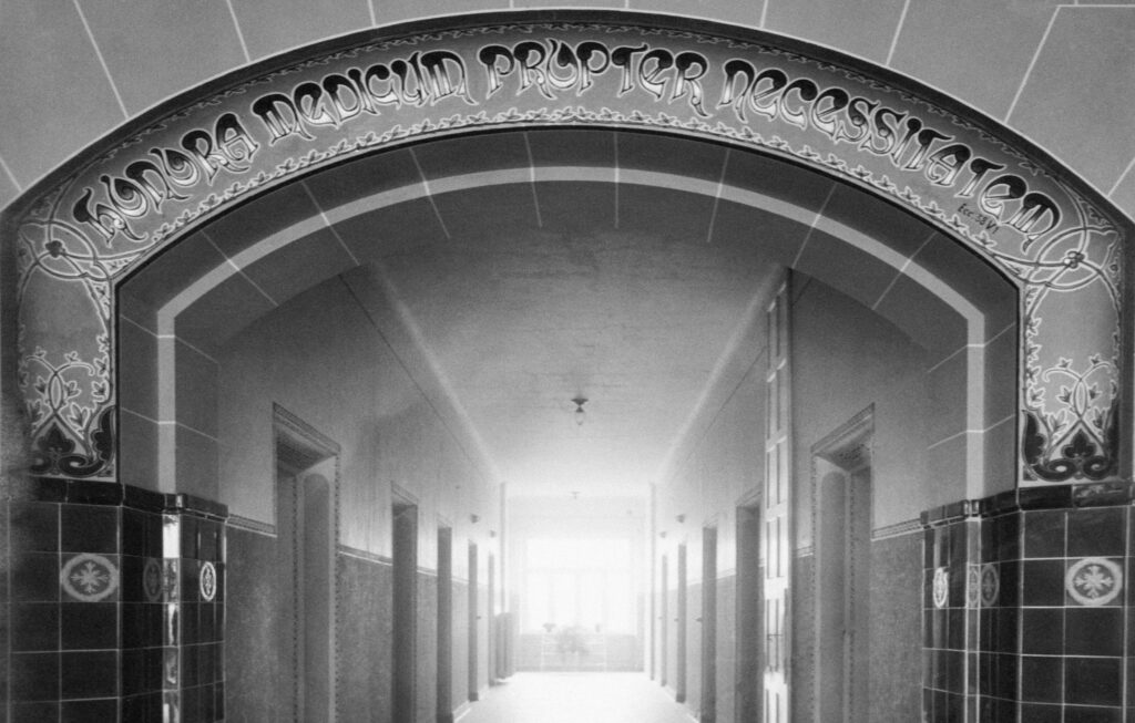 Bild vum Haaptgang an der Zithaklinik um Reiz de chaussé. Hei waren di grouss Poliklinik an d’Radiologie amenagéiert. Am Jugendstil goufen hei d’Wänn an de Bou iwwert den Gang gestalt.D’Schreift heescht: HONORA MEDICUM PROPTER NECESSITATEM ( Honorez le médecin pour le besoin).Des glaséiert Faïencerien sinn deelweis nach erhalen, leien awer ënnert engem Gipsbotz den bei enger Renovatioun doriwwer gemaach ass.Den Deel vum Gebai gehéiert zu deenen eelsten vun der Klinik. D’Bild ass vum Paul Kutter Fotograph zu Letzebuerg.