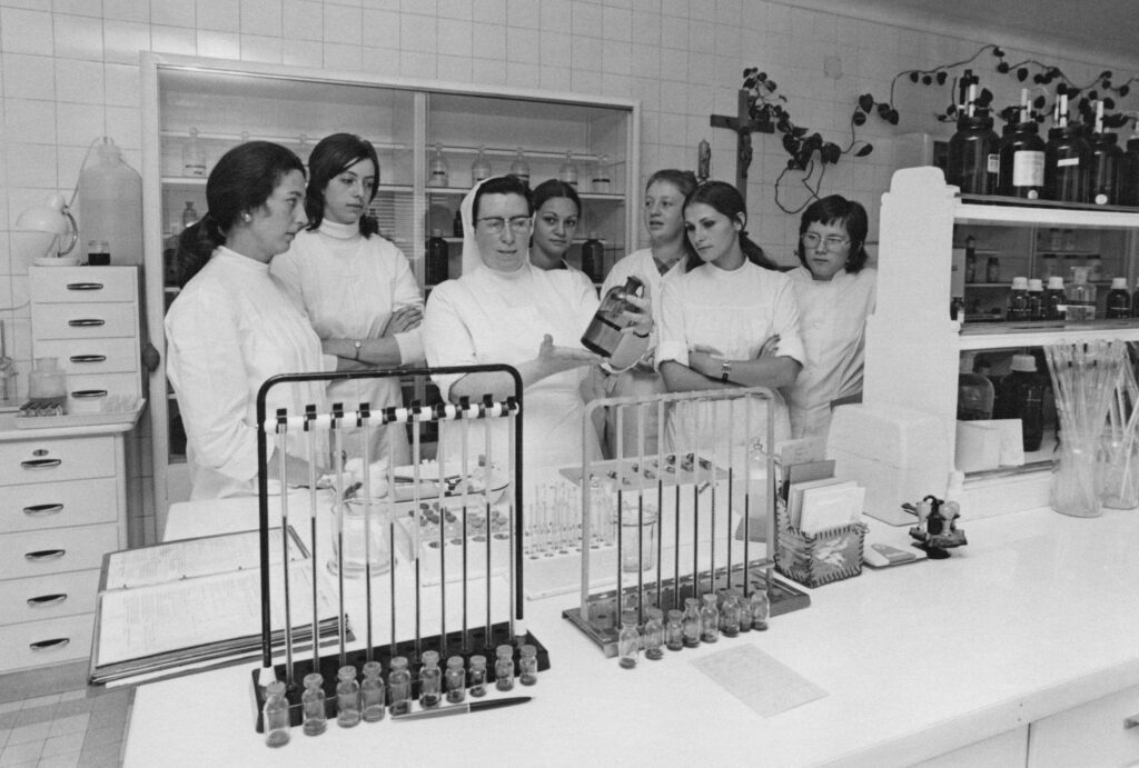Bild aus dem Laboratoire vun der Zithaklinik.Mir gesinn hei eng Schoulschwester( Schwëster Marie Etienne) déi Soignantsschülerinnen weist wei Verdënnungen vun Laboratoireflessegkeeten gemaach gi. Di mäscht Laboratoireennersichungen sinn manuell gemaach gi. Verschidden Analysen sinn nëmmen 1-2 mol an der Woch gemaach gi.All Soignants huet missten déi normal Wäerter aus dem Blutt an dem Urin kennen, an déi mäscht Analysen verstoen an maachen kennen.Mir gesinn hei eng sougenannten Bludsenkungsapparatur wou gekuckt gëtt ob der Patient eng Infektioun huet. Spéider konnt eng Soignante sech am Fach Laboratoire spezialiséieren an am Laboratoire schaffen. Haut sinn déi mäscht Analysen voll automatiséiert. Vill Analysen kennen och vum Patient selwer gemaach gi.(Bluttzockerwäerter, Gerennungswerter, Härzwerter...). D’Bild ass vum Jean Weyrich Fotograph am Luxemburger Wort