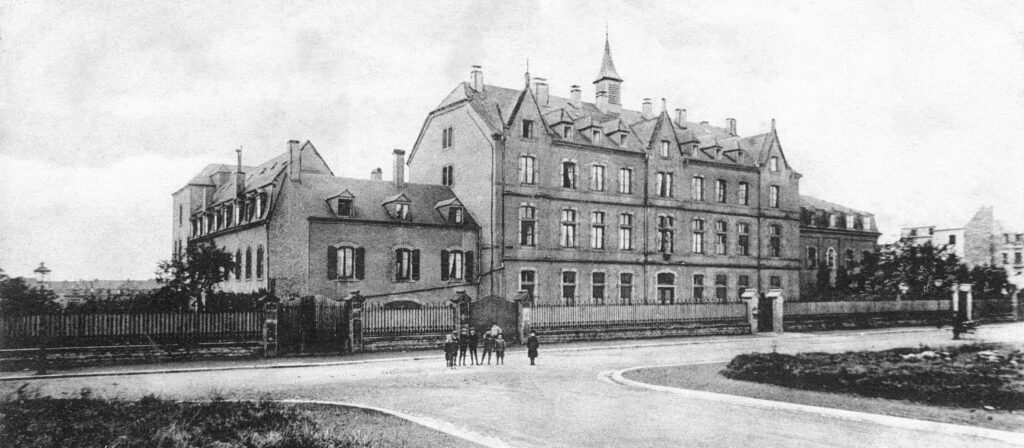 Bild vun dem Zithakloschter aus der ganz fréier Zäit. D’Gebai vum Klouschter, wei ob der Photo, steet haut och nach. Lenks a riets sinn awer de Bau vun der Klinik( 1925 ) an en Altersheim derbäi komm. De ganze Hollerecher Quartier war deemools nach eng eegen Gemeng, huet sech rasant entwéckelt, den Uschloss an en Eisebunnsnetz huet Lëtzebuerg international vernetzt, de Quartier Hollerech ass mat Brécken verbonnen gi, de Krich huet gewisen dat eng adequat Versuergung vun Verletzten néideg war. Aus engem Uerden deen sech em jonk Meedercher bekëmmert huet, hunn d’Schwësteren erkannt wat gebraucht gi ass , an sech an dësem Quartier niddergelooss.Wou ob der Photo nach Wisen a Perche waren sin modern Wunnhaiser , Firmen a Butteker entstanen, d’Avenuen sinn gebaut gi.Deemools sinn et an der Nopeschgemeng Lëtzebuerg 4 Klinicken gi( Saint Francois, St Joseph, Ste Elisabeth an Eich.) Am Ufank hat d’Klinik 40 Better. D’Gebaier vun der Klinik hunn sech permanent an deenen neien Ufuerderungen an Methoden adaptéiert, et sinn vill Dokteren no hirer Ausbildung hei hin schaffe komm, d’Klinik an den Orden vun de Schwesteren ass permamanet gewues. D’Gebaier bestinn haut och nach. Den Photograph as net bekannt. D’Postkaard as am Besetz fum Henri Kugener.