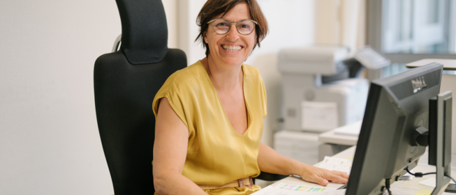 Photo d'une dame souriante à son poste de travail devant son ordinateur