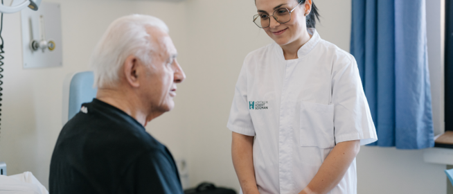 Foto einer Pflegerin der SRH und ihres Patienten im Zimmer, lächelnd