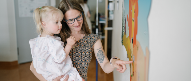 Foto einer Mutter im Krankenhaus mit ihrem Kind in der Kinderstation, die ihm ein an der Wand angefertigtes Fresko zeigt