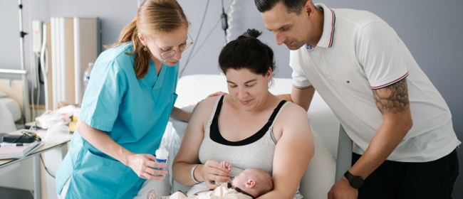 Foto einer Pflegerin, die ein Paar und sein Neugeborenes im Zimmer der Entbindungsstation der Bohler-Klinik begleitet.